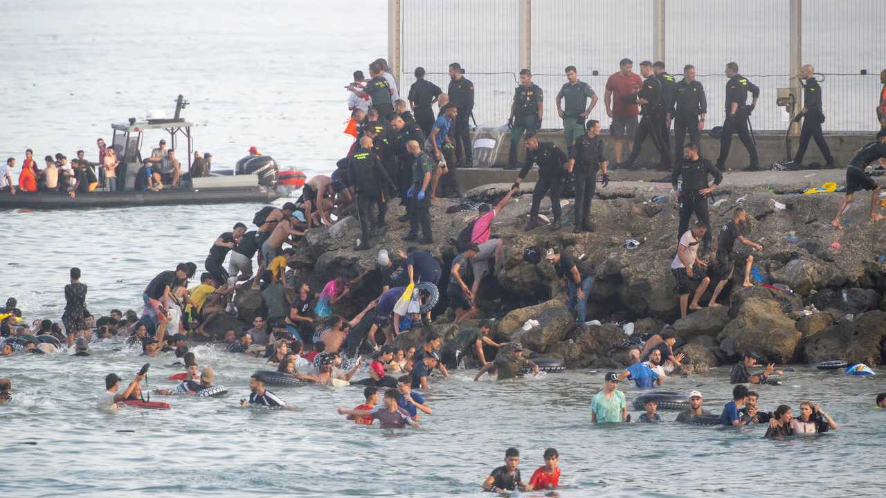 Menschen versuchen an der spanisch-marokkanischen Grenze bei Ceuta über Felsen und durch das Wasser zu gelangen, während Einsatzkräfte am Ufer stehen