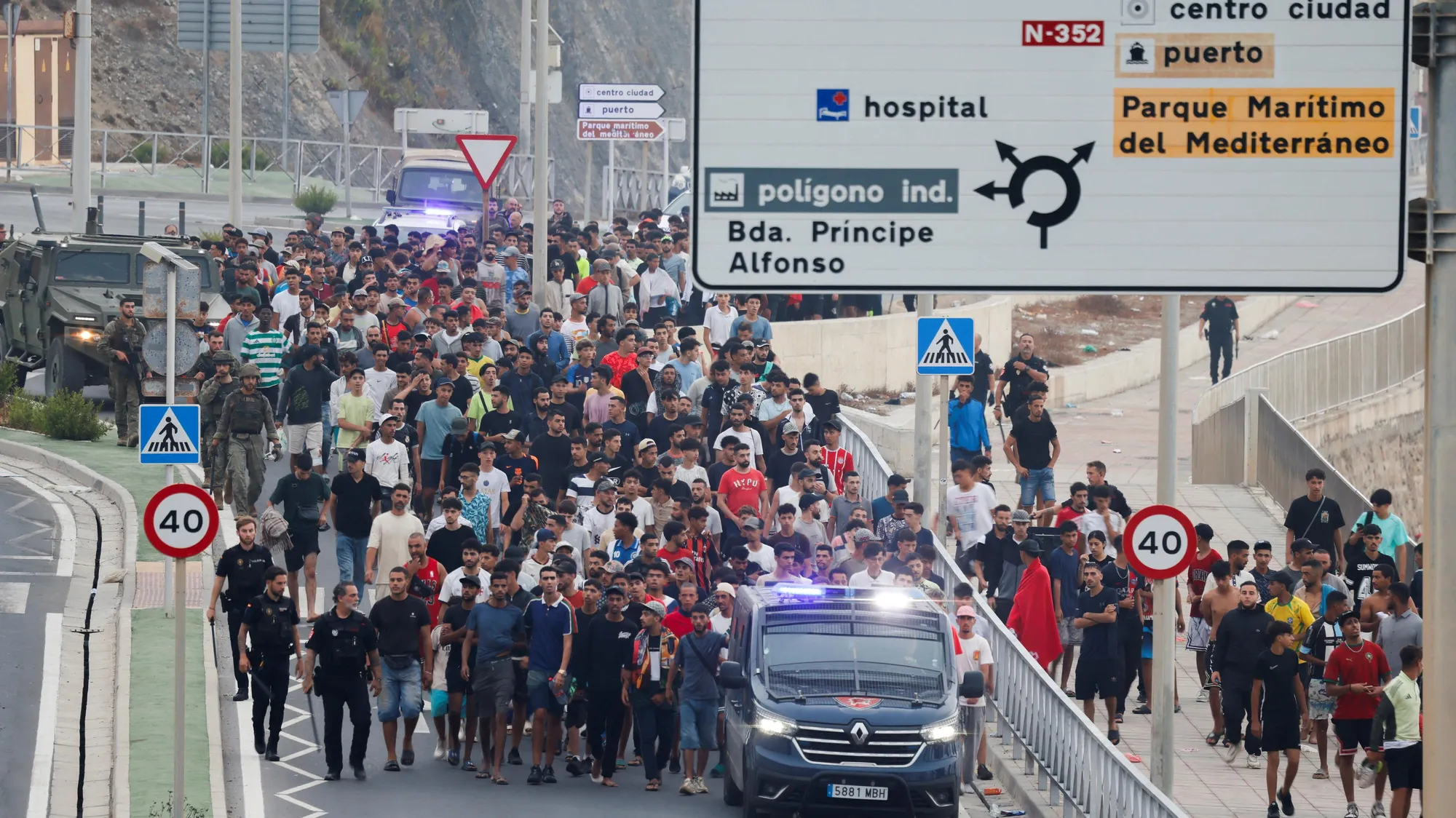 Eine große Menschenmenge bewegt sich in Ceuta unter Polizeibegleitung entlang einer Straße Richtung Stadtzentrum